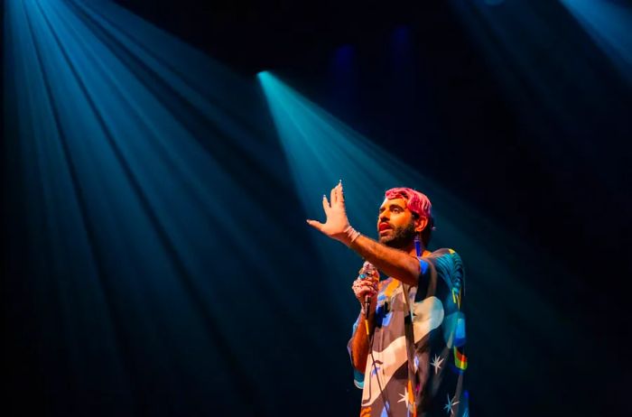 Alok stands on stage with a microphone, illuminated by blue spotlights.