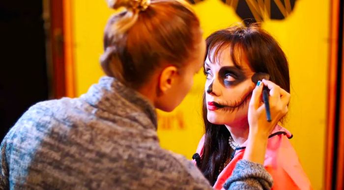 A makeup artist creates a chilling look on a brunette woman for a Halloween celebration.