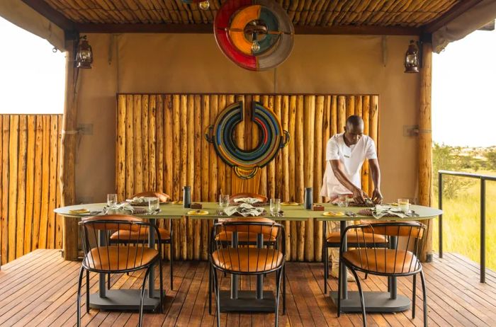 The dining area at Singita Mara River Tented Camp is beautifully arranged on a wooden platform outdoors, complete with wooden seating.