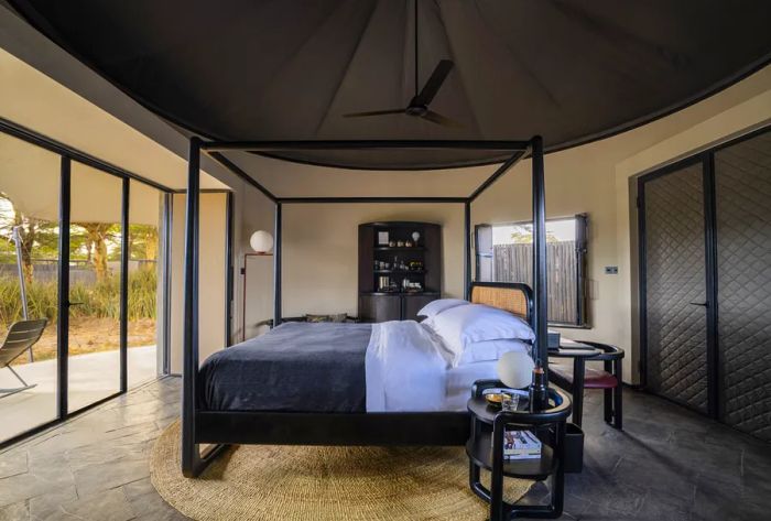 This guest suite at Angama Amboseli features a four-poster bed, elegant stone floors, and sliding doors that open to a private veranda.