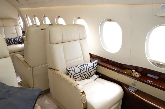 Two white leather chairs positioned back to back, adjacent to a row of windows within a private jet.