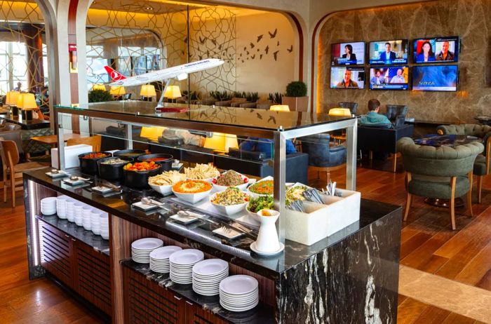 A buffet setup at the Turkish Airlines Lounge in Washington Dulles Airport, featuring a wall lined with TV screens in the background.