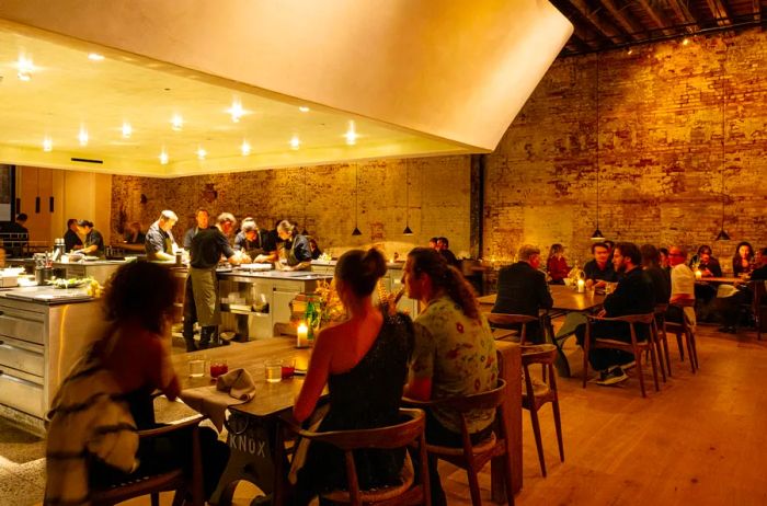 Intimate dining groups at tables with chefs visible in an open kitchen behind them