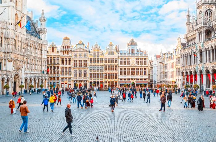 Individuals stroll through the central Grand-Place in Brussels, Belgium, surrounded by historic architecture.