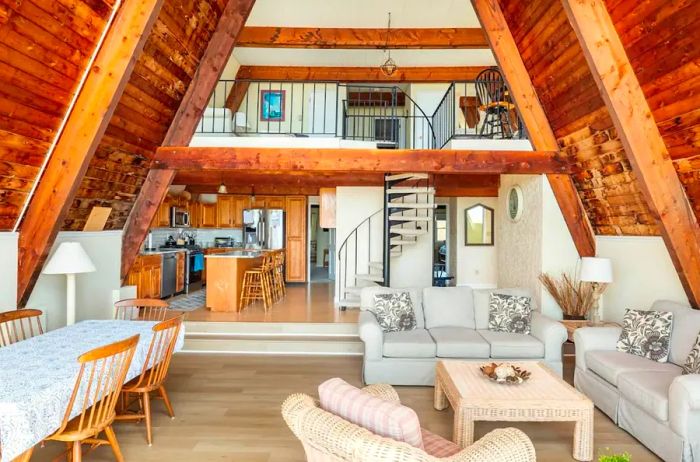 A multi-level living and dining area adorned with wooden and white furnishings, with the kitchen and a spiral staircase visible in the background.