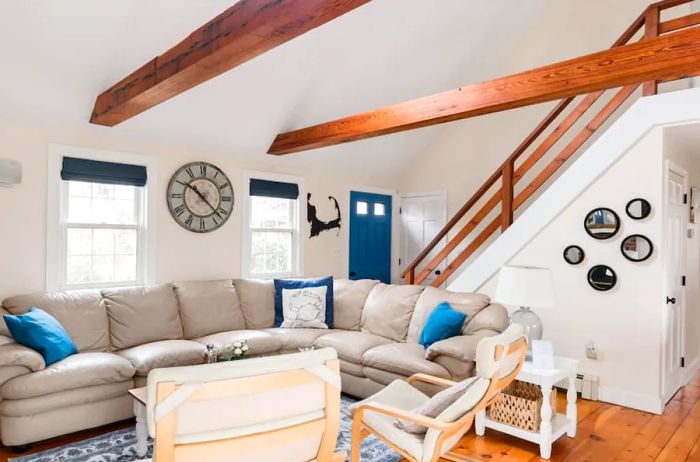 Living room showcasing an L-shaped gray sofa, rustic wood beams, and staircase leading to the upper floor