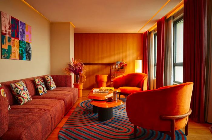 A glimpse of the guest room at the SO/Paris hotel, featuring a long orange sofa, two plush orange chairs surrounding a coffee table, and a vibrant rug.