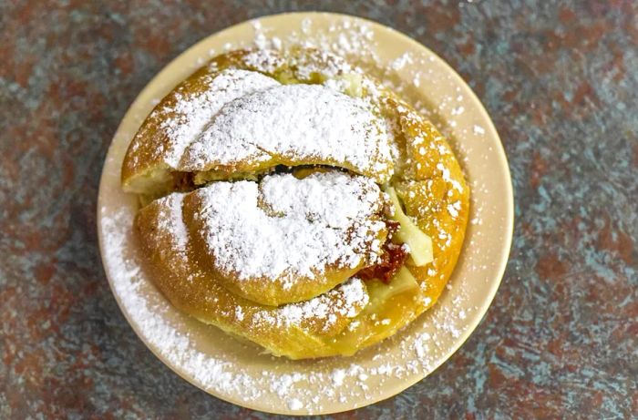 A round mallorca, a soft roll dusted with powdered sugar, on a plate