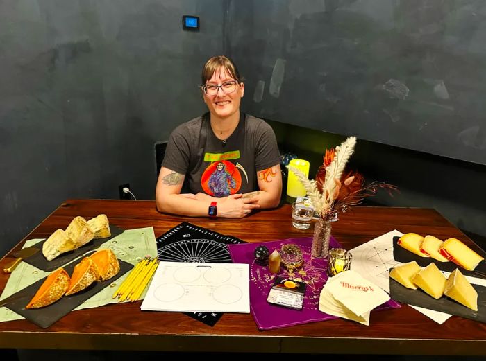 Jennifer Billock, a skilled tyromancer, is seated at a dark wooden table surrounded by a selection of four cheeses.