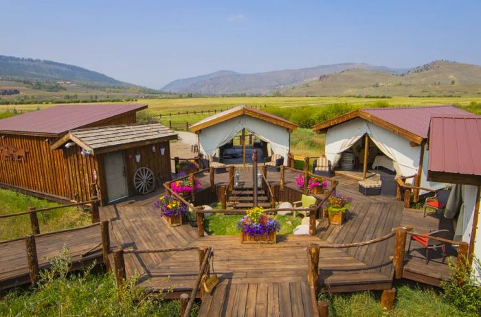 Surrounded by a charming wooden deck adorned with flower-filled tubs, the Lazy U Spa features three white massage tents along with a cozy wooden building.