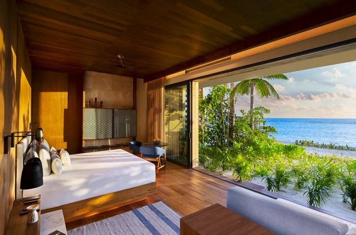 A sea-view guest room at Banyan Tree Mayakoba features wooden flooring and expansive sliding glass doors opening to the beach.