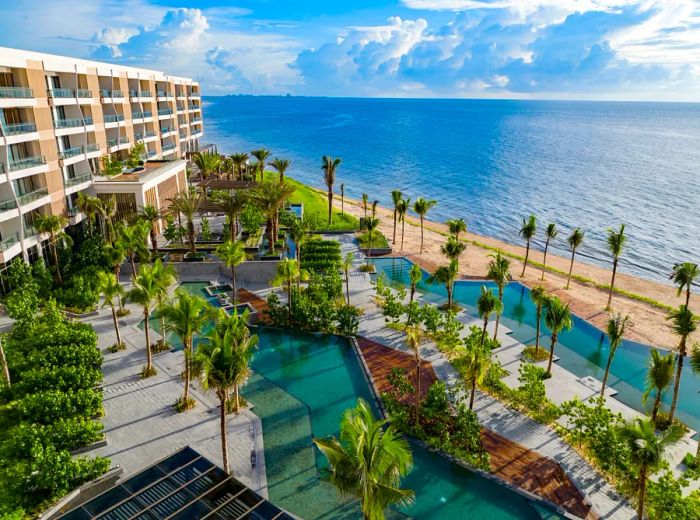 Aerial view of Waldorf Astoria Cancun next to the ocean, featuring two long asymmetrical pools surrounded by palm trees.