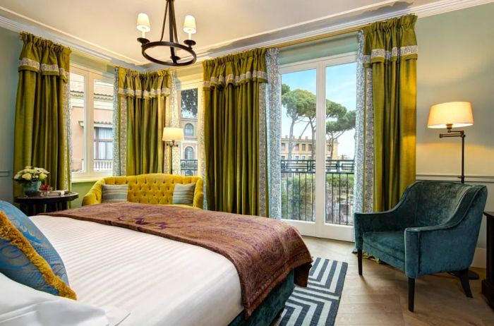 A Junior Suite bedroom at Hotel de la Ville in Rome features hardwood floors, expansive curtains and windows, and a mustard-colored sofa.