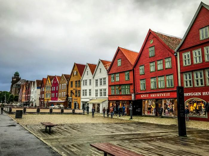 A line of historic wooden storefronts in shades of white, brown, rust, and mustard yellow, featuring A-frame roofs, in Bergen, Norway