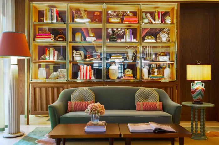 The lobby features a green velvet sofa, two lamps, small tables, and a wall lined with bookshelves at Hôtel Barrière Fouquet's New York.