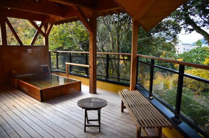 A private onsen situated on a wooden deck with a roof, overlooking the forest