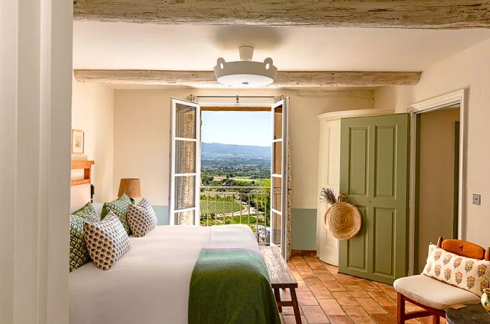 Interior of a beige and green guest room featuring French windows that open to reveal the lush countryside at Hôtel Crillon le Brave.