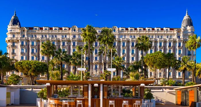 The exterior of the grand Carlton Cannes, a Belle Époque-era structure, framed by palm trees.