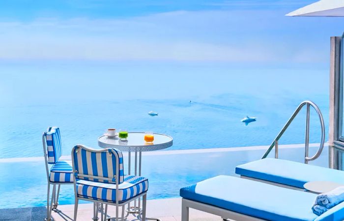 A view of the Mediterranean from the terrace of the duplex pool suite at the Maybourne Riviera, featuring two blue-and-white striped chairs at a small round table and two blue lounge chairs.