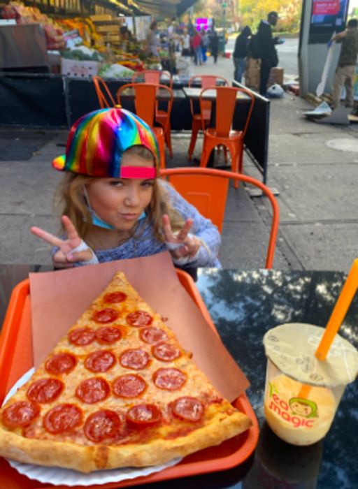 Maya flashes peace signs with her fingers while posing with a massive slice of pepperoni pizza.