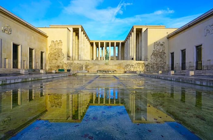 The exterior of the Palais de Tokyo, featuring a rectangular shallow pool that beautifully reflects the building.