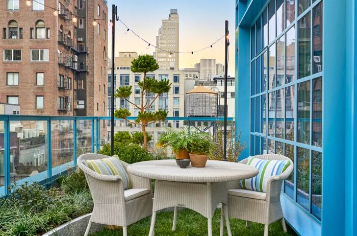 The terrace of suite 909 features two white wicker chairs and a small round table, surrounded by plants and offering views of the skyscrapers.