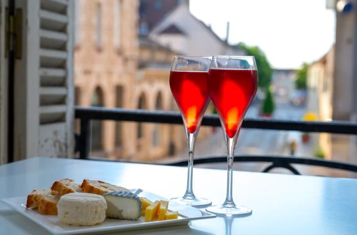 Enjoying a Kir Royal, a French aperitif cocktail made with crème de cassis and topped with champagne, typically served in flute glasses, while overlooking a charming old French village.