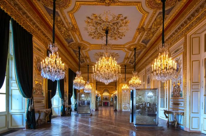 An ornate gold and white hallway adorned with mirrors and chandeliers, reminiscent of a miniature Versailles.