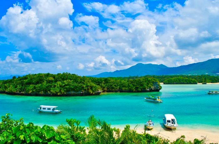 A few small boats glide through the crystal-clear waters around Ishigaki Island in Iriomote Ishigaki National Park, alongside pristine sandy beaches.