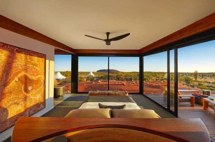 The Dune Pavilion Bedroom at Longitude 131 boasts floor-to-ceiling windows that provide stunning views of the surrounding rust-colored landscape.