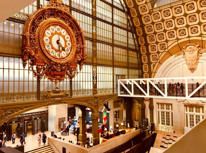 A large, ornate gold clock adorns the wall of small glass windows inside the Musée d'Orsay.