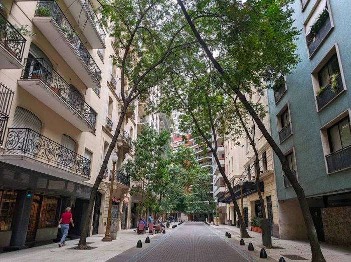 Arroyo Street in Buenos Aires, Argentina: a narrow, winding cobblestone road lined with lush green trees and elegant white French-style buildings featuring wrought-iron balconies.