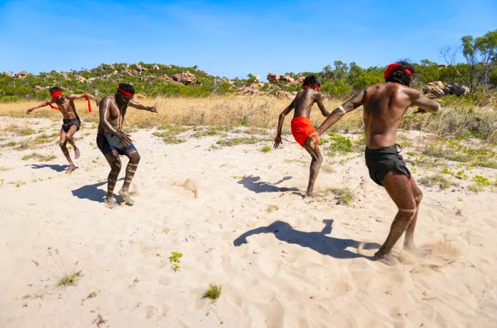 Four Wunambal Gaambera Traditional Owners in Western Australia performing a dance on the sand.