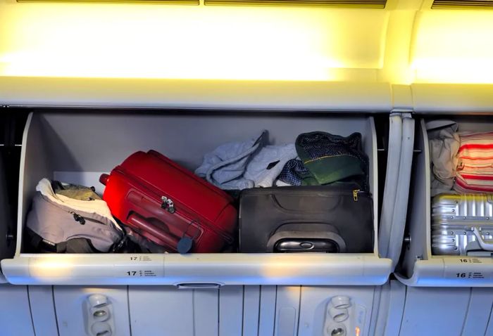 Black and red rolling suitcases along with smaller carry-on and personal items stored in an airplane's overhead compartment