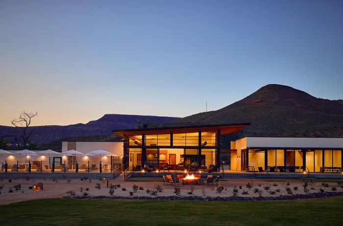 Outside the AutoCamp Clubhouse, a mid-century modern structure, at night, featuring a firepit with a roaring fire in front.