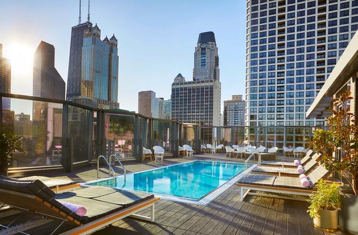 The outdoor pool at the Viceroy Chicago features a wooden deck and a few unoccupied lounge chairs, offering stunning views of the surrounding skyscrapers.