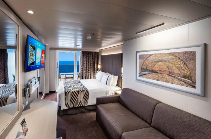 Interior of an MSC World Europa Balcony Cabin featuring a seating area, bed, and TV.