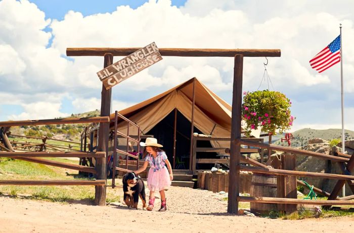 A child dressed as a cowboy walks alongside a dog beneath the Lil Wrangler Clubhouse sign at Brush Creek Ranch.