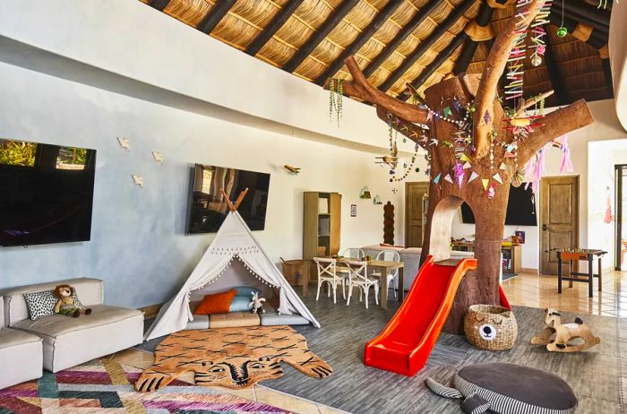 Interior view of the Tortuguitas kids club at Esperanza featuring play areas, a faux tree with a slide, a tent, and relaxation and sitting spaces.