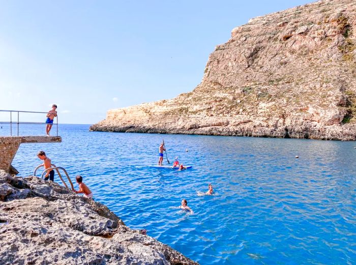 People enjoying swimming and paddleboarding in a cove along Gozo's coast, Malta.