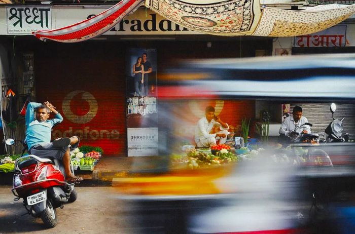 Individuals resting on motorcycles near a fruit stall.