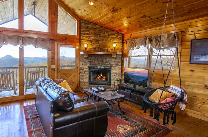 Interior view of a cabin featuring a leather sofa, a cozy fireplace, and expansive windows that frame the mountain landscape