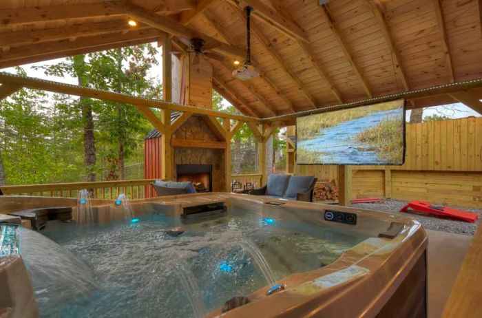 Streams of water cascade in a spacious hot tub, complete with a roof, a large screen, and a cozy fireplace.