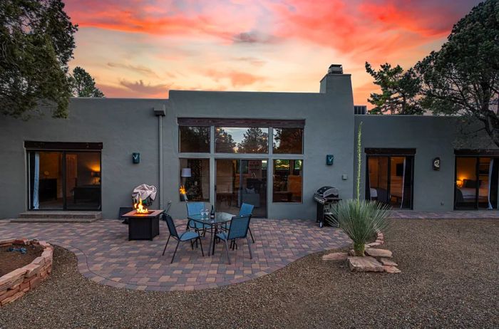 A backyard scene showcasing a pink sunset sky, complete with a firepit and a small outdoor table surrounded by chairs.