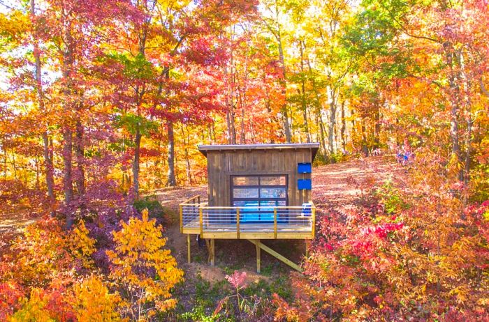 Exterior view of a quaint cabin with a porch, nestled among trees adorned in fall colors