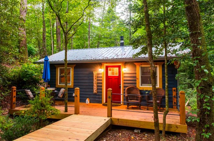 A wooden deck graces the front of the Georgia cabin, featuring a red door and surrounded by lush trees.