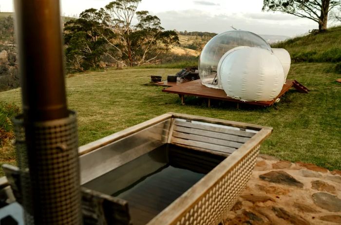 Outdoor wood-fired hot tub with a bubble tent set against the backdrop of the Australian countryside