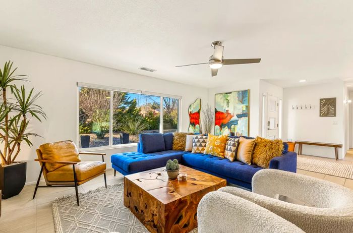 A stylish living room featuring a tufted blue sectional sofa, a leather armchair, and a cube-shaped wooden table, complemented by a spiky desert plant in the corner.