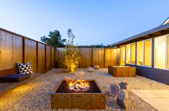 A cozy firepit surrounded by gravel and a wooden fence at dusk