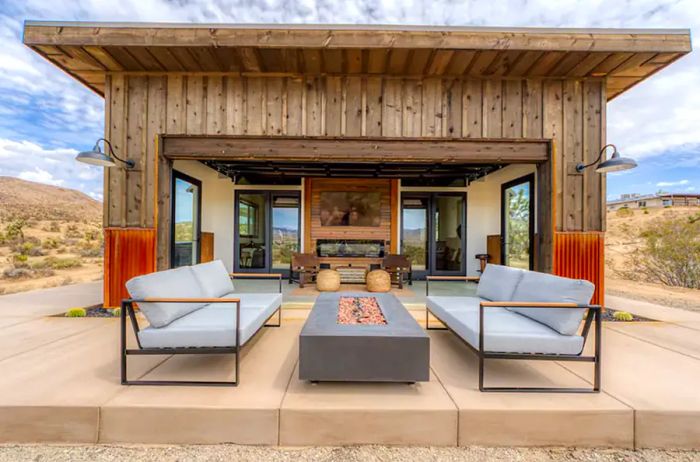 Wooden cabin with a cement porch featuring two sofas facing a firepit